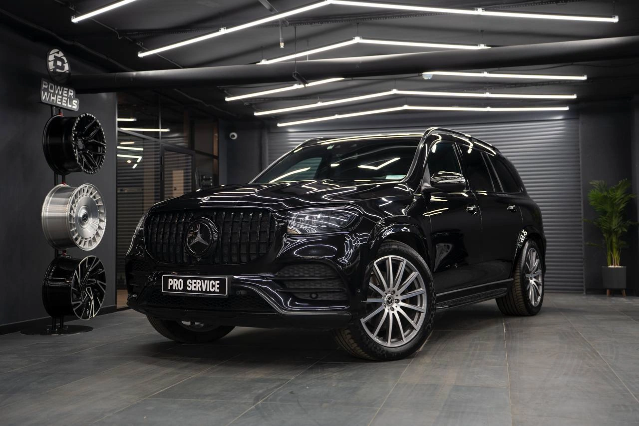 Чёрный Mercedes GLS, вид спереди под углом: хромированная решётка, крупные колёса и отражения света на кузове.