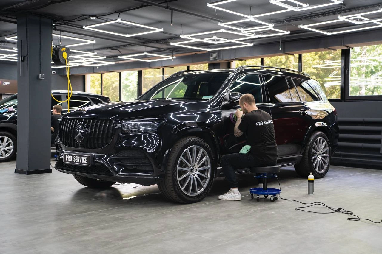 Мастер полирует боковую часть чёрного Mercedes GLS у передней двери, сидя на рабочем стуле.