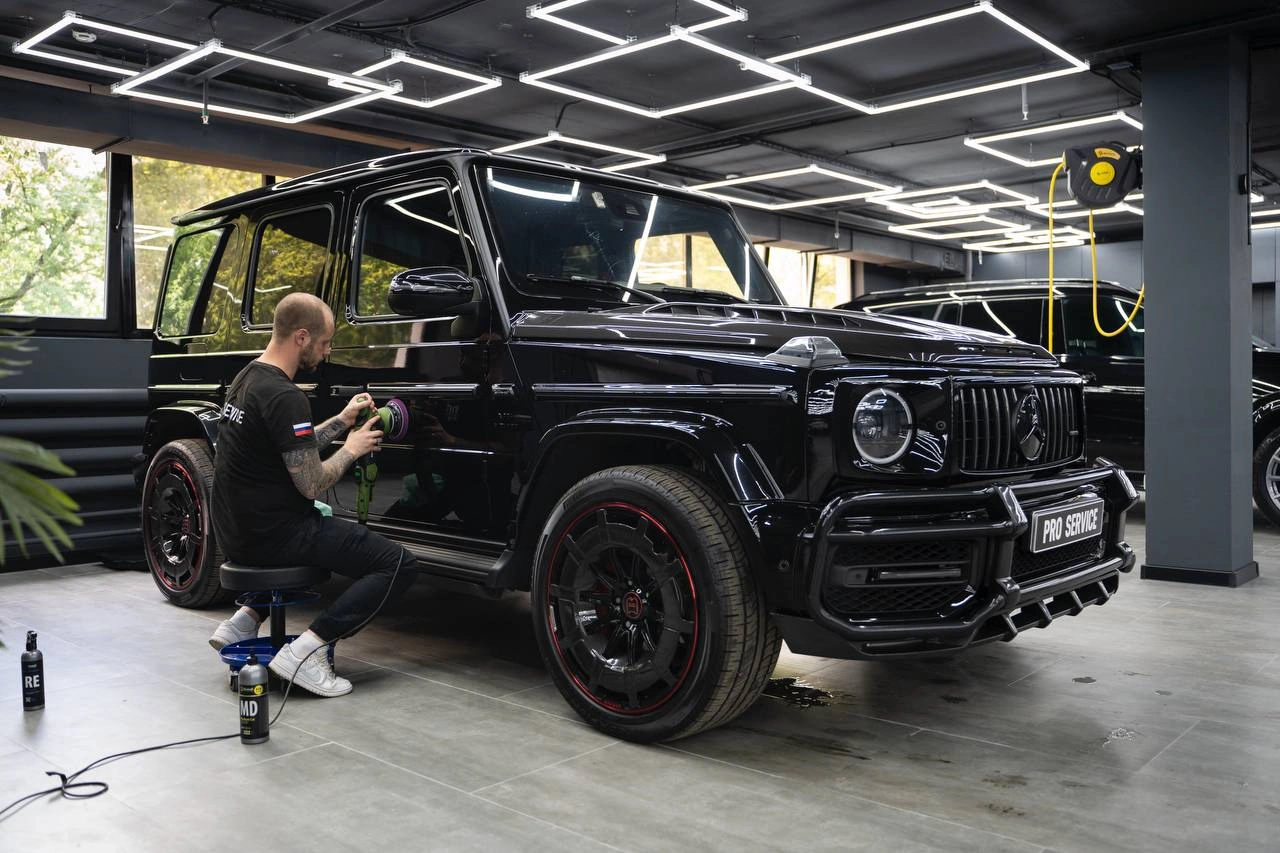 Мастер полирует боковую панель чёрного Mercedes-Benz G-class AMG машиной с небольшим круглым диском.