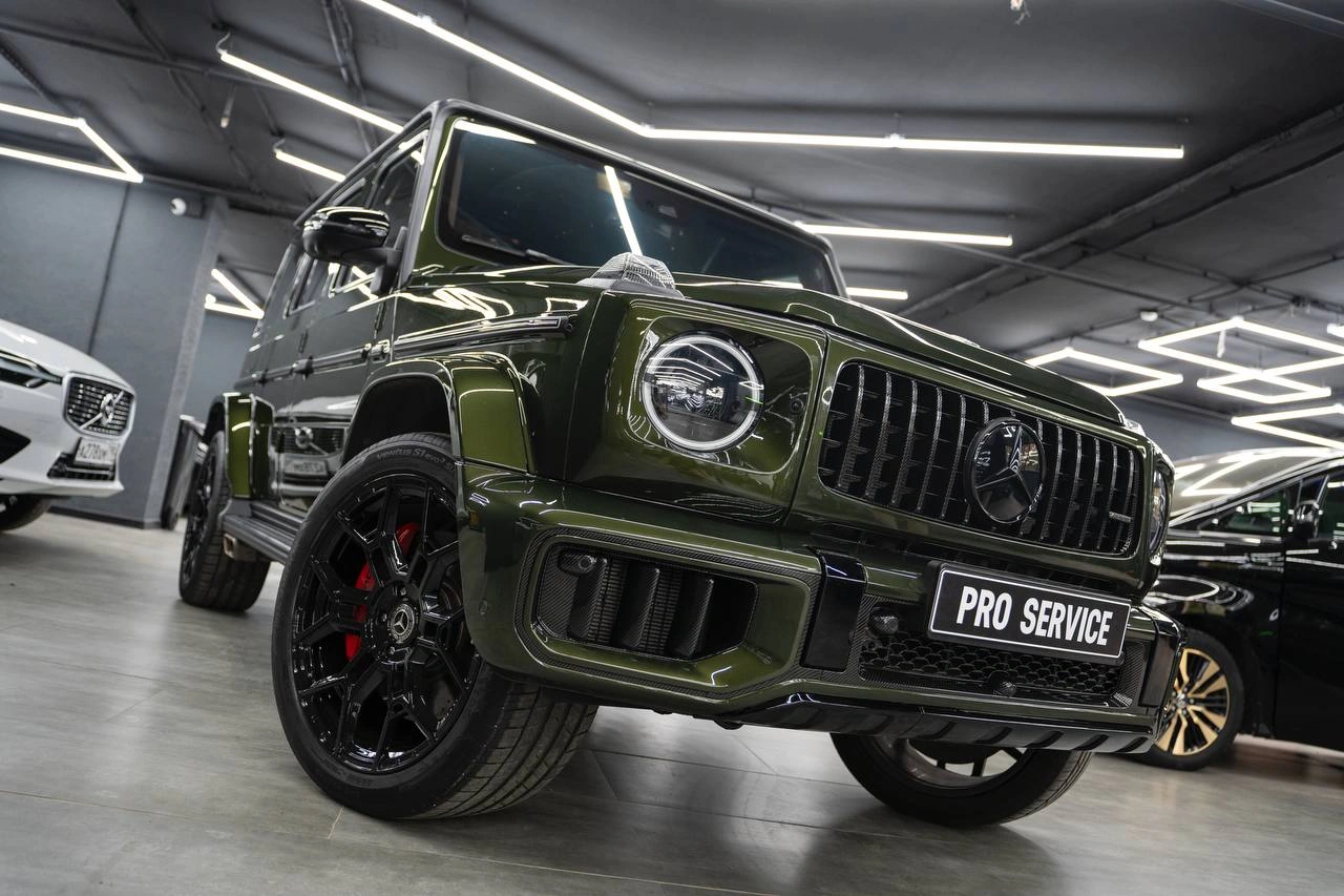Тёмно-зелёный Mercedes-Benz G63 AMG с чёрной решёткой и красными суппортами, вид спереди с низкого ракурса.