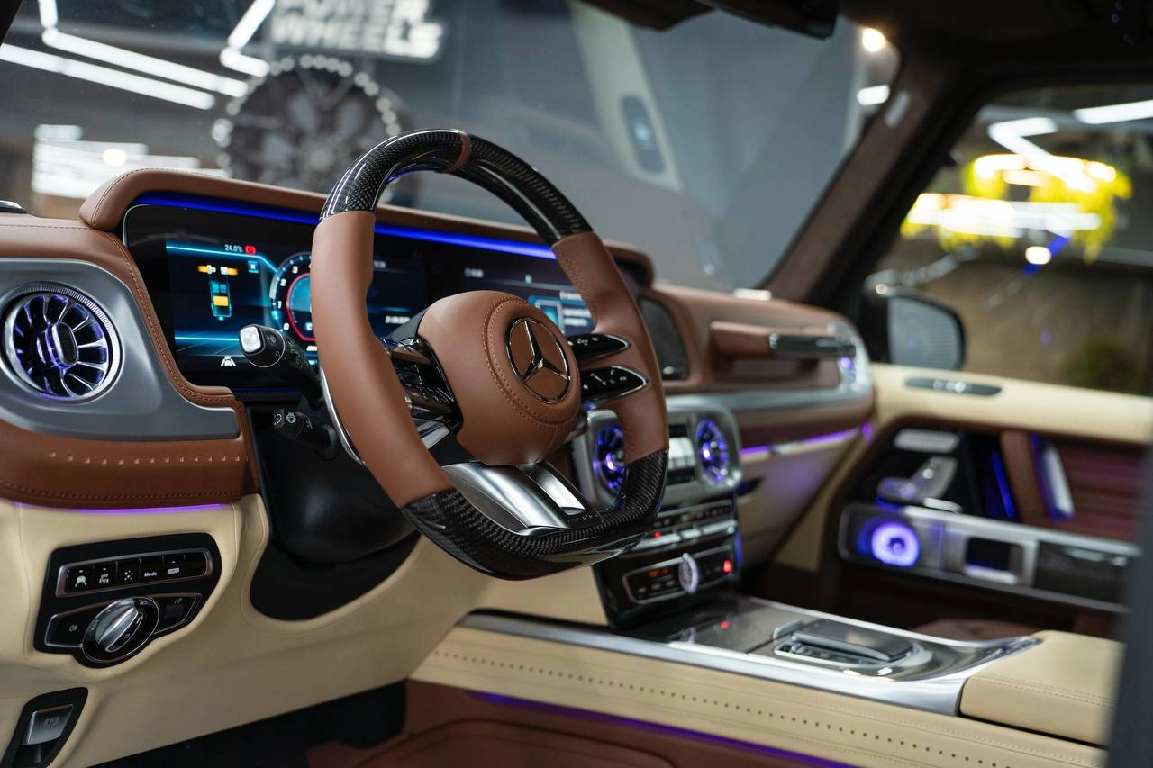 Салон Mercedes-Benz G63 AMG: коричневый руль, цифровая приборная панель и фиолетовая подсветка.