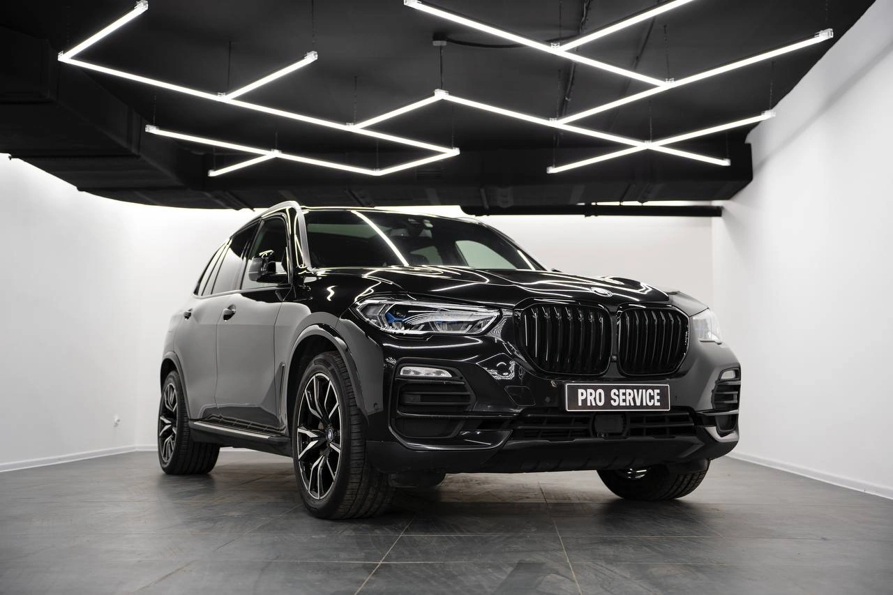 Чёрный BMW X5 в светлом боксе: вид спереди и сбоку, крупная решётка радиатора и тёмные колёсные диски.