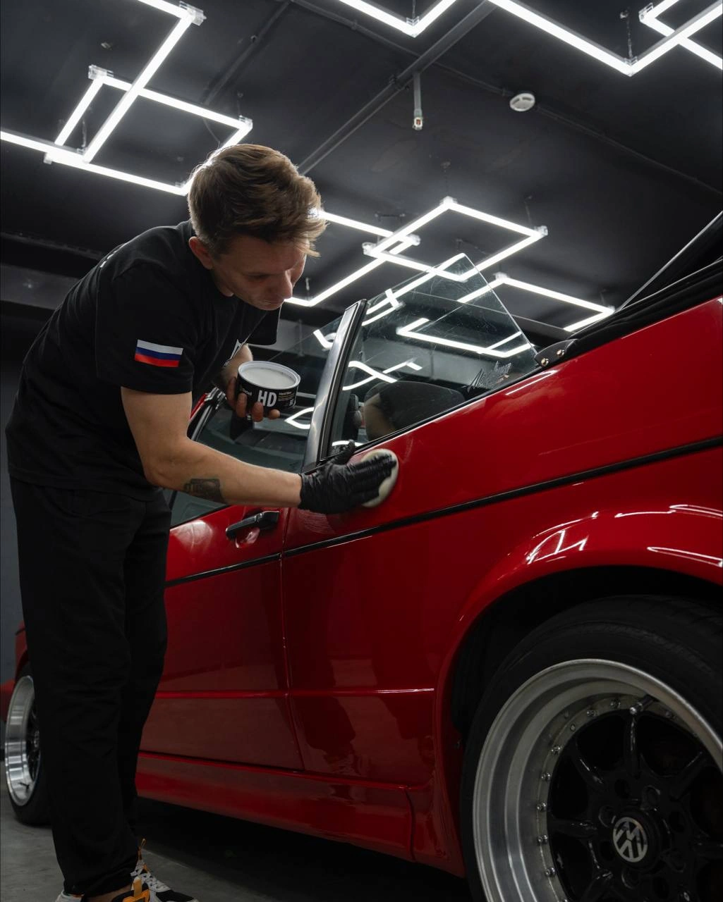Мастер протирает дверь красного Volkswagen Гольф 1 кабриолет микрофиброй.