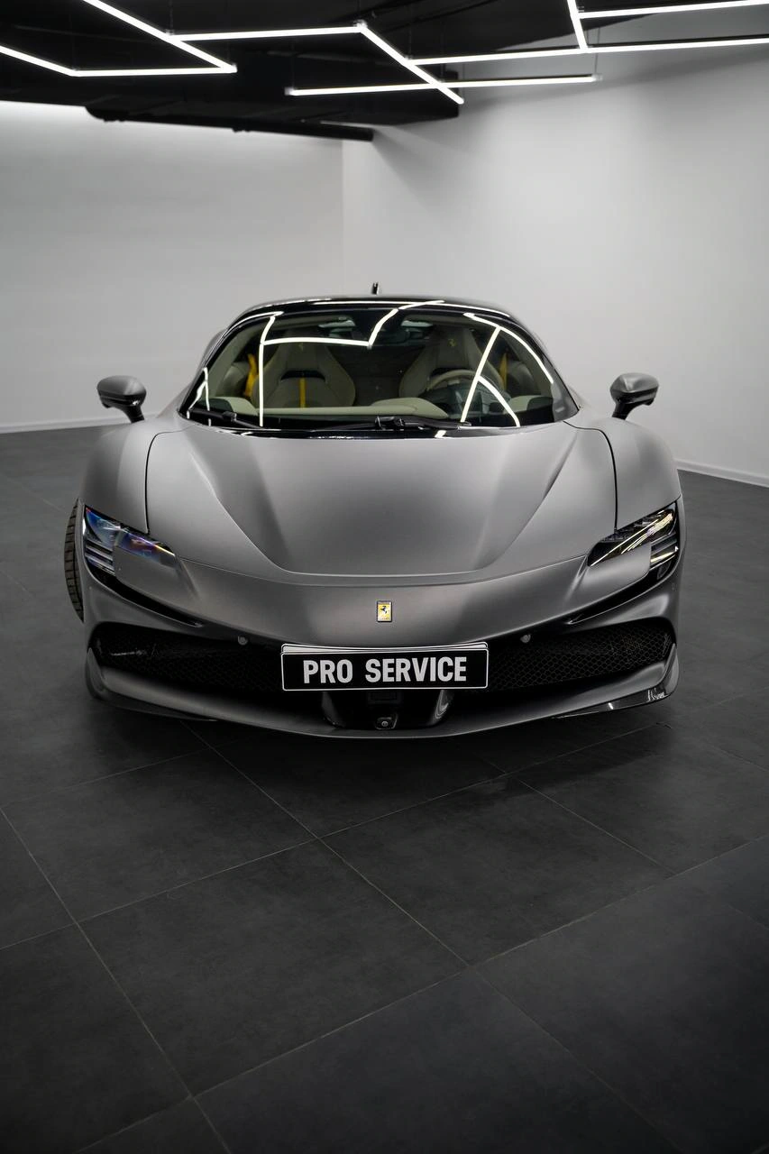 Ferrari SF90 Stradale — серый спорткар спереди с симметричными фарами и эмблемой на капоте