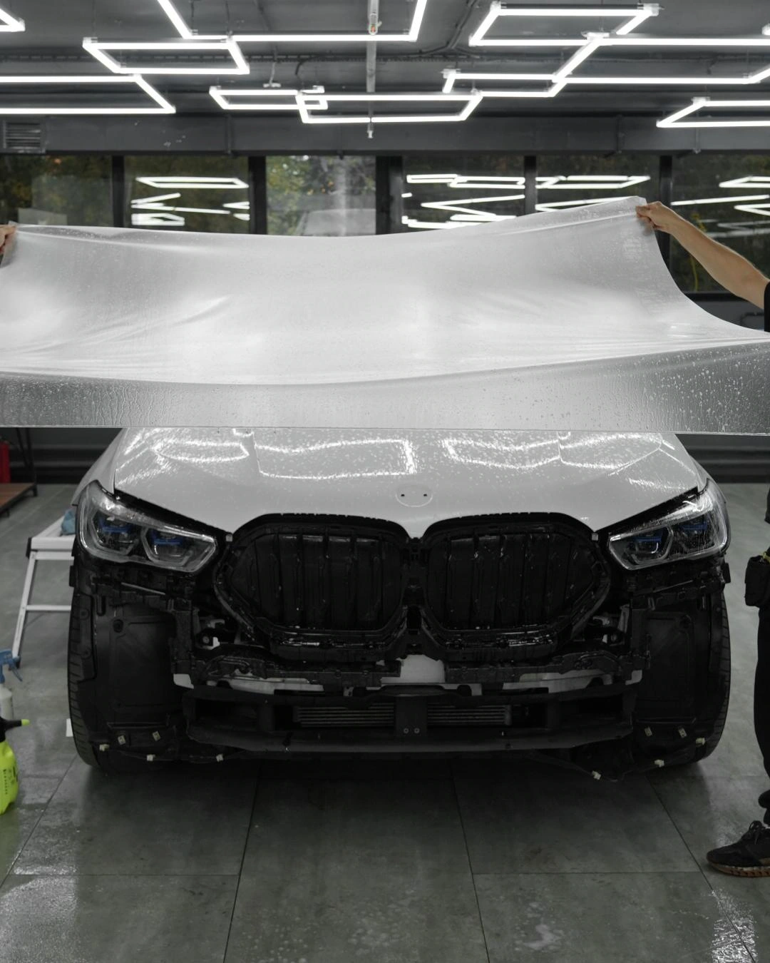 BMW X6 в процессе оклейки: плёнка на капоте, передний бампер снят, открыты внутренние элементы передней части.