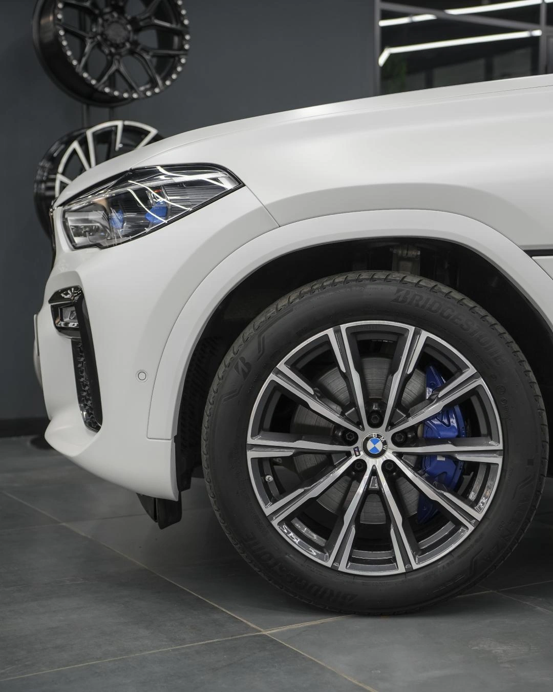 Переднее колесо и белое крыло BMW X6 крупным планом: за светлыми спицами диска виден синий суппорт.