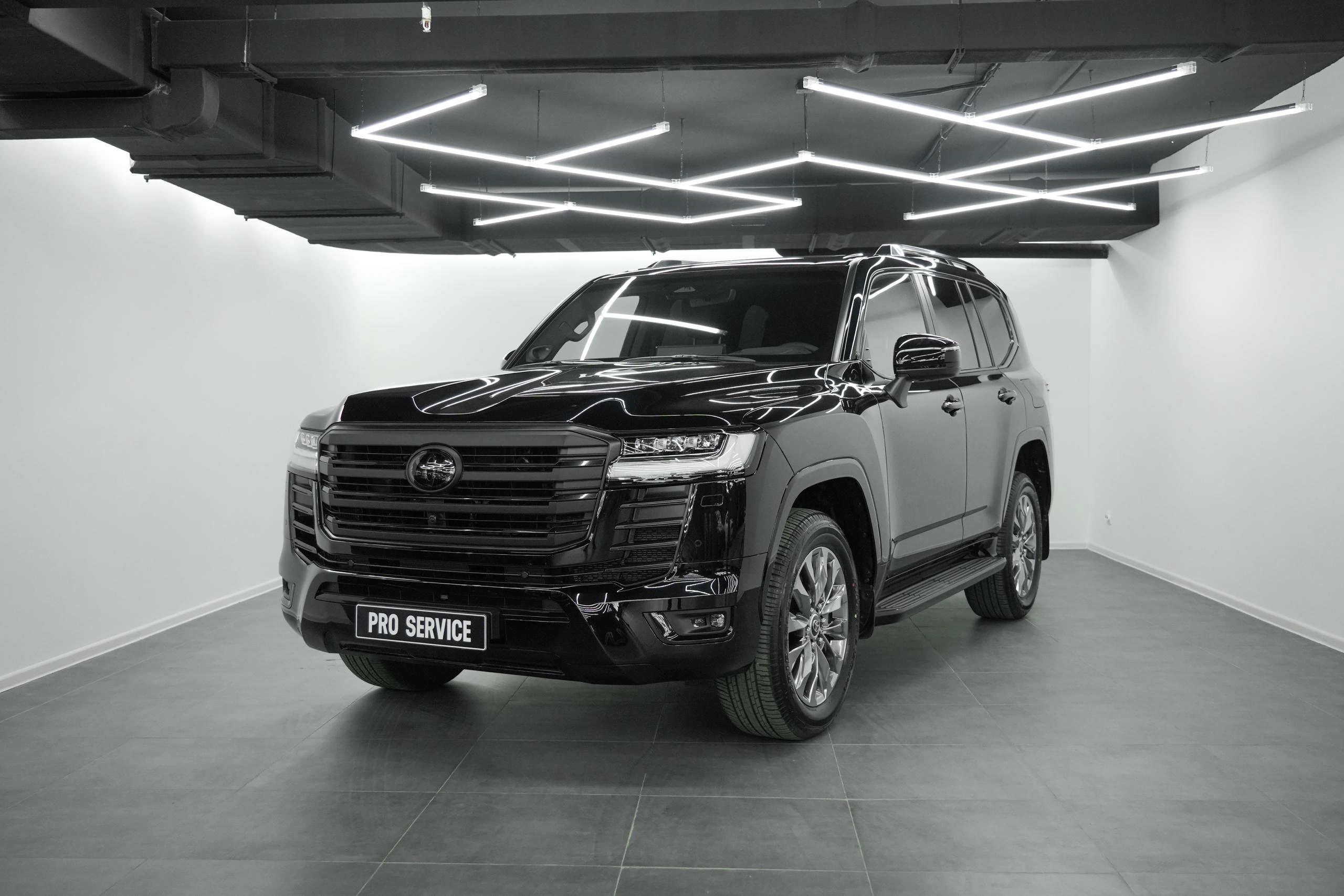 Toyota Land Cruiser — чёрный внедорожник с крупной решёткой радиатора в светлом рабочем боксе
