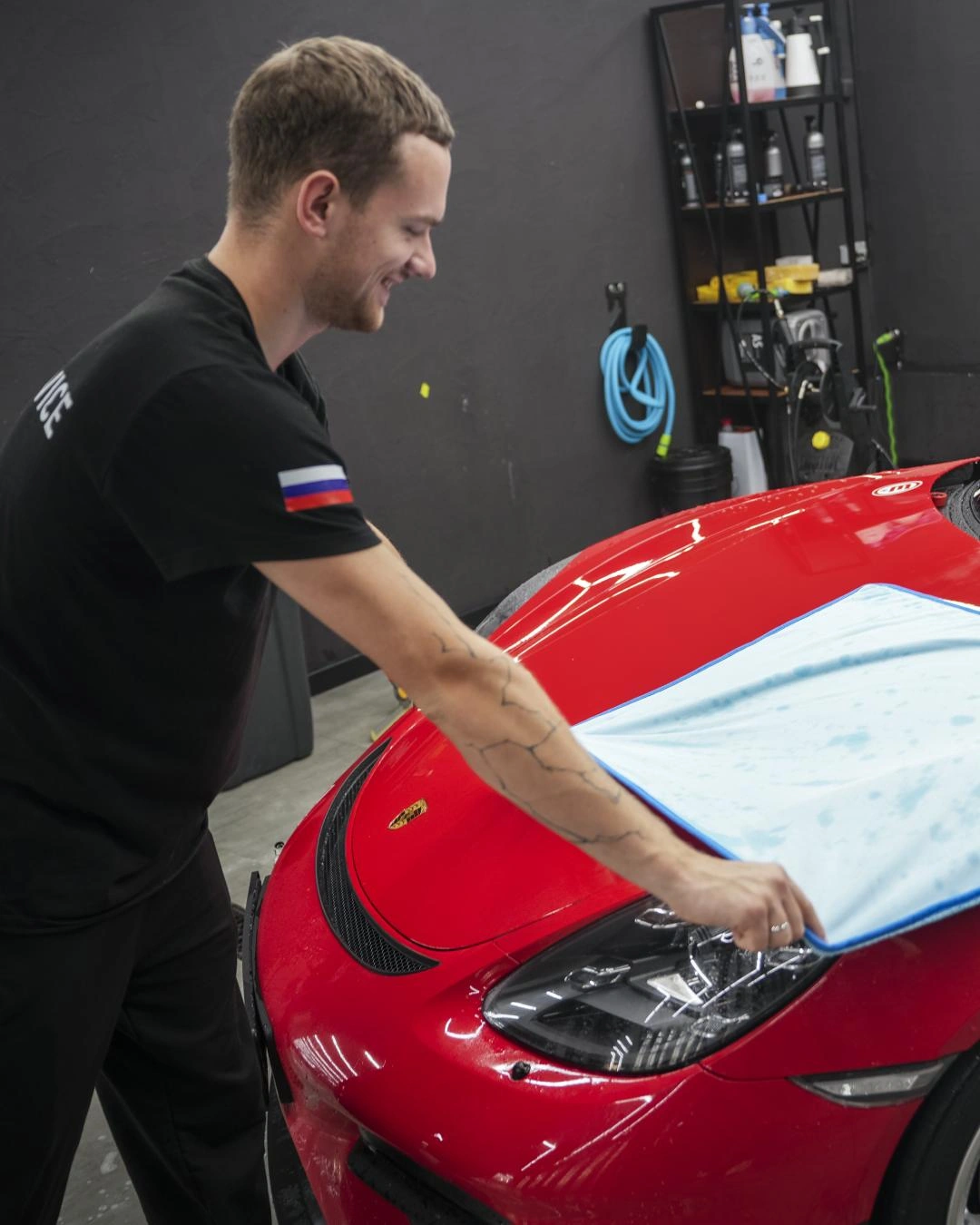 Мастер протирает капот красного Porsche Cayman GT-4 большой голубой микрофиброй.