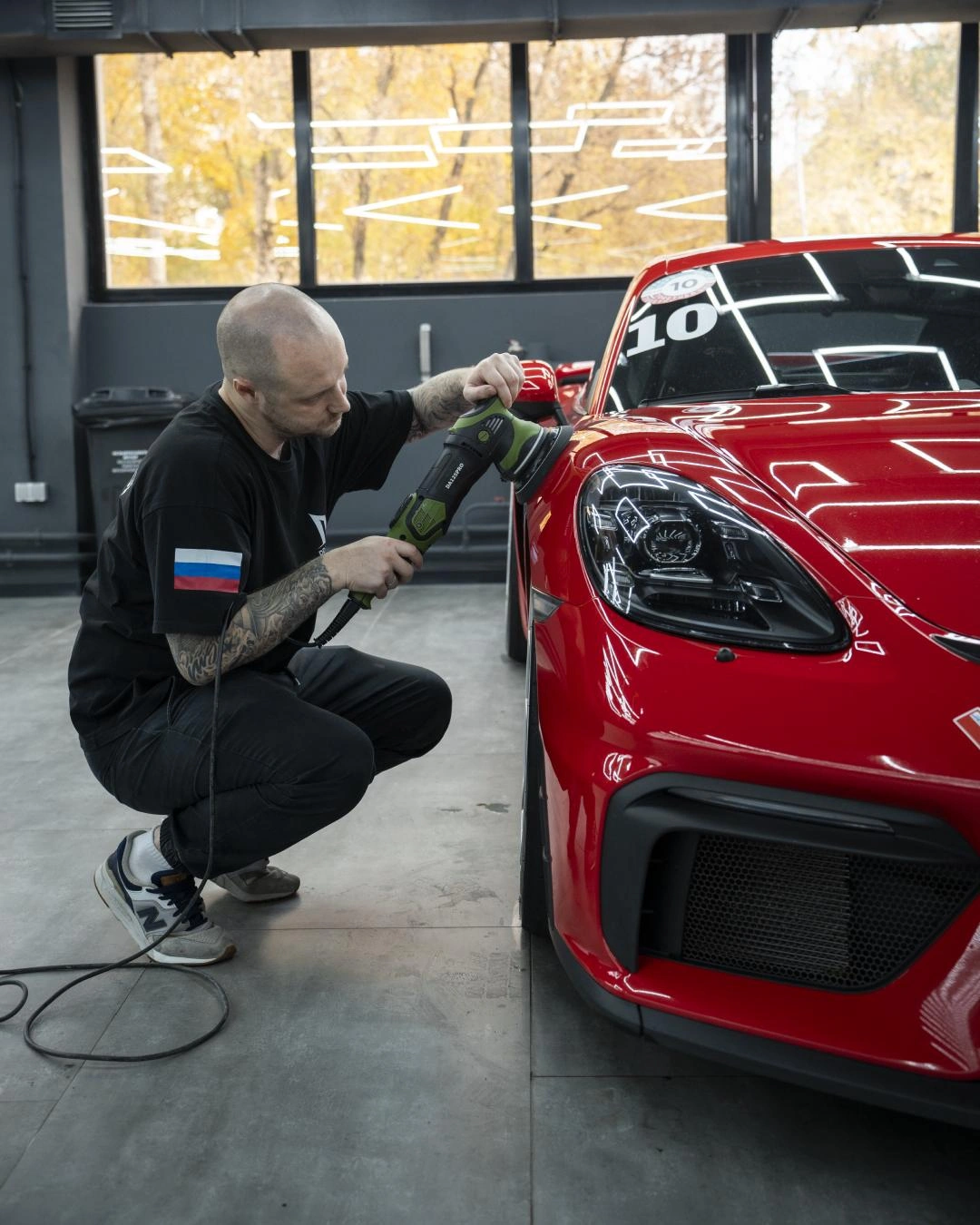 Мастер полирует переднее крыло Porsche Cayman GT-4 машинкой рядом с фарой.
