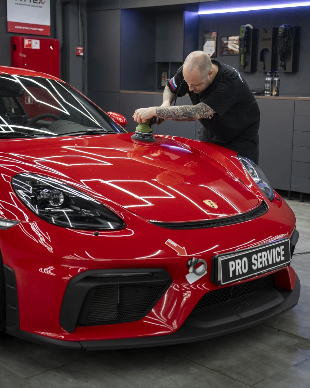Полировка капота Porsche Cayman GT-4: мастер работает машинкой по красной поверхности кузова.