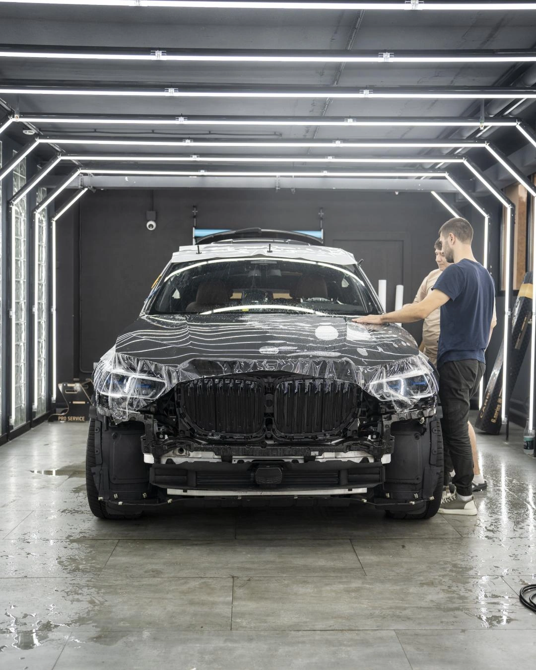 BMW X5 со снятым передним бампером во время оклейки капота, прямой вид спереди.