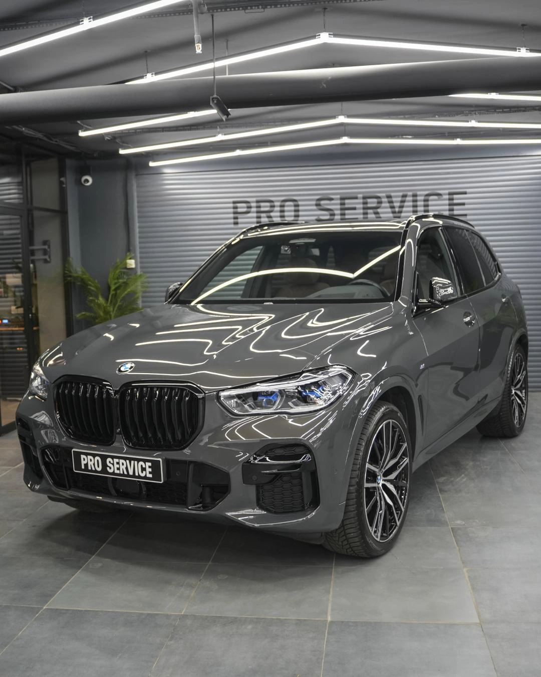 Серая BMW X5 с отражениями световых линий на кузове, вид спереди под углом в студии.