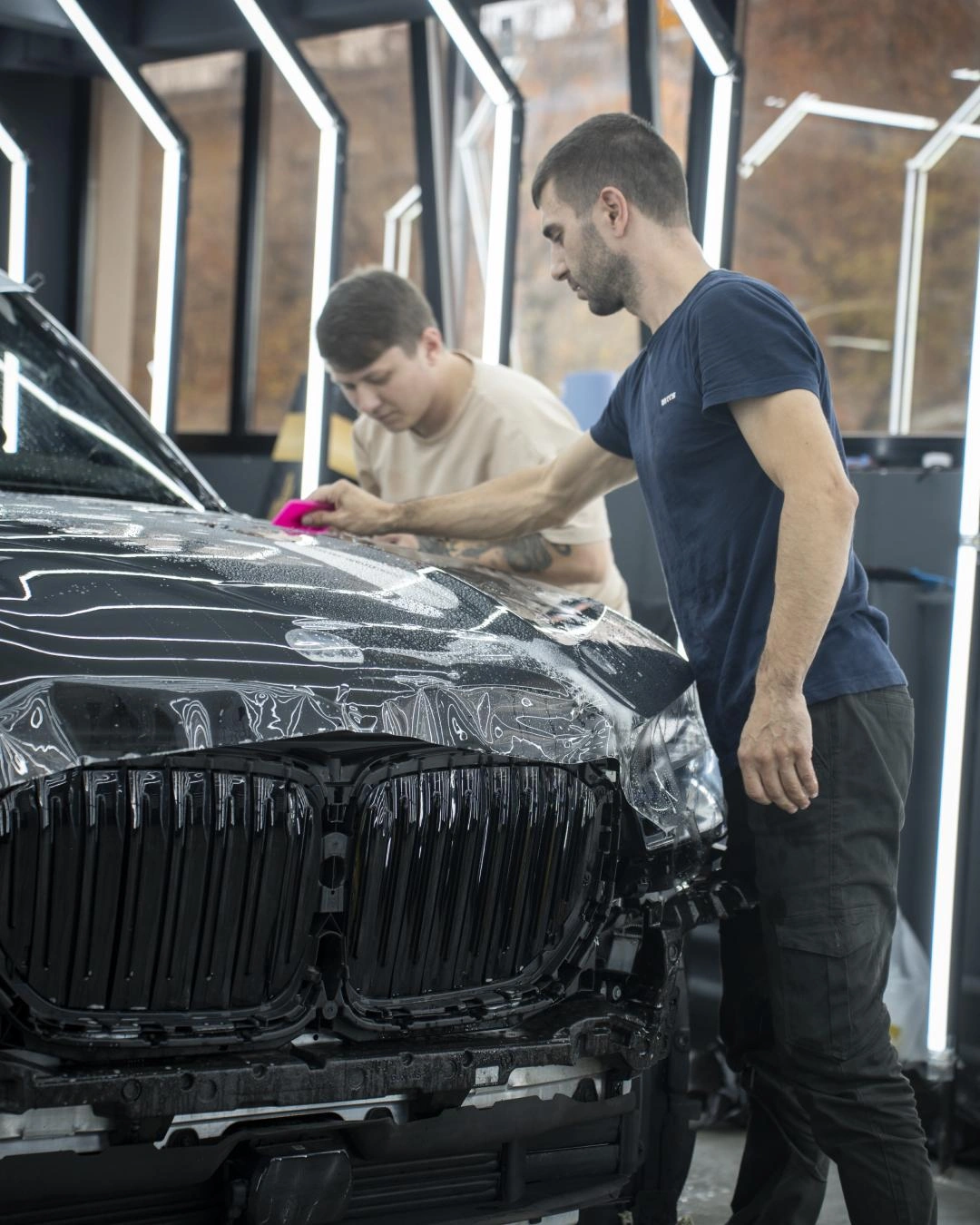 BMW X5 при оклейке капота: мастера работают с прозрачной плёнкой у передней части кузова.
