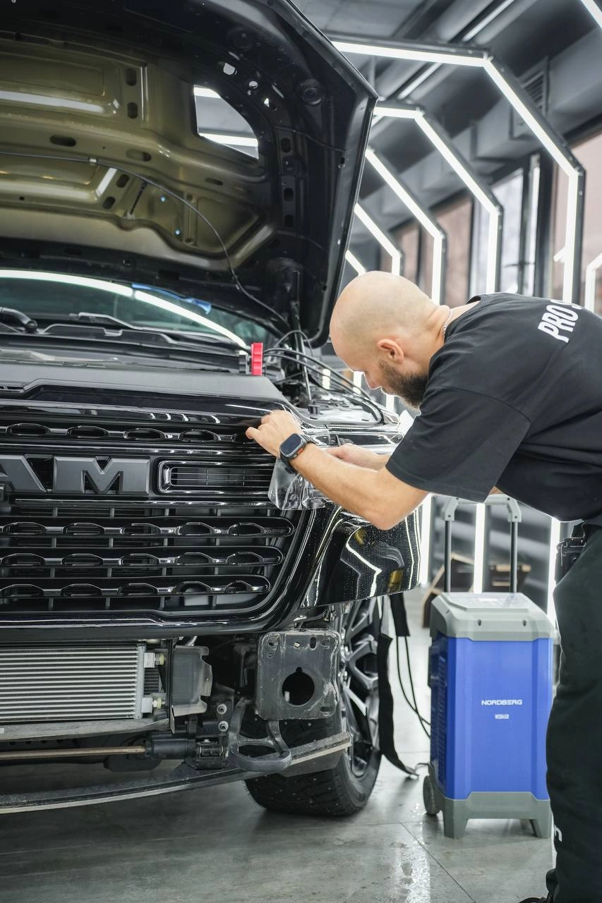 Мастер разглаживает защитную плёнку на фаре и передней части Dodge Ram.