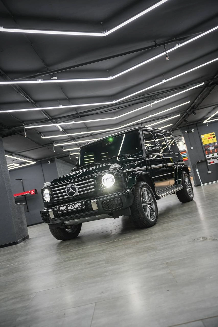Mercedes-Benz G-Class — чёрный внедорожник с включёнными фарами, вид спереди под углом