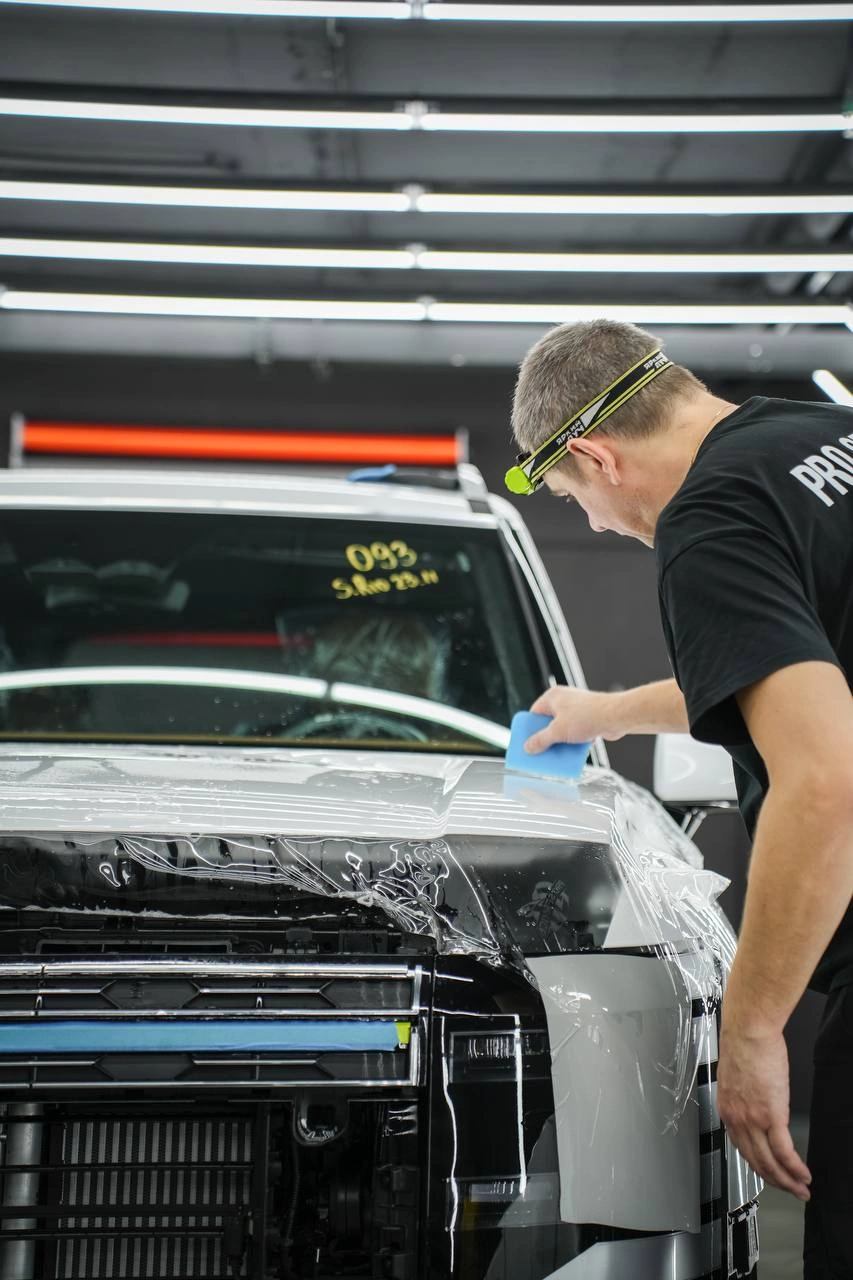 Оклейка передней части Hyundai Palisade: мастер разглаживает полиуретановую плёнку.