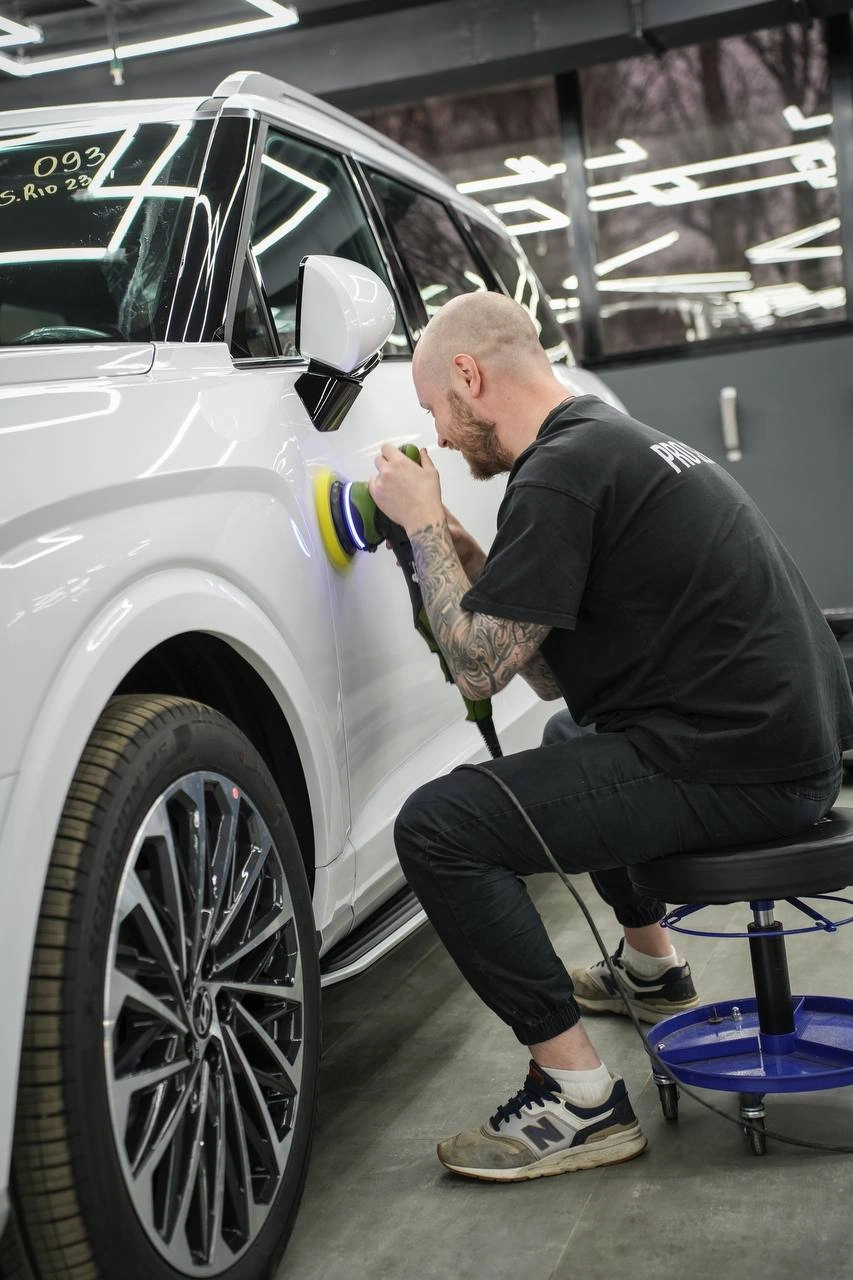 Мастер полирует боковую панель Hyundai Palisade рядом с передним колесом.