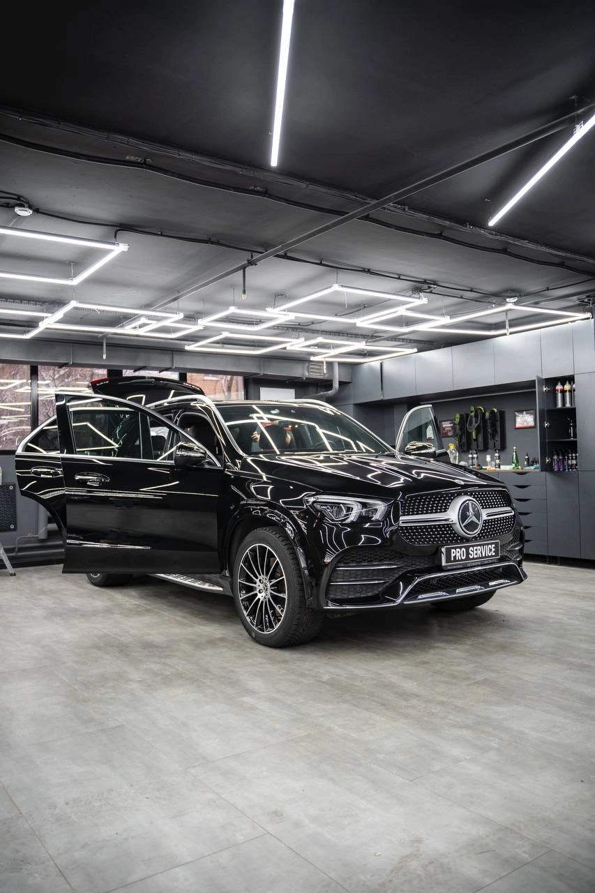 Mercedes-Benz GLE в студии с открытой передней дверью: вид спереди и сбоку на тёмный кузов.