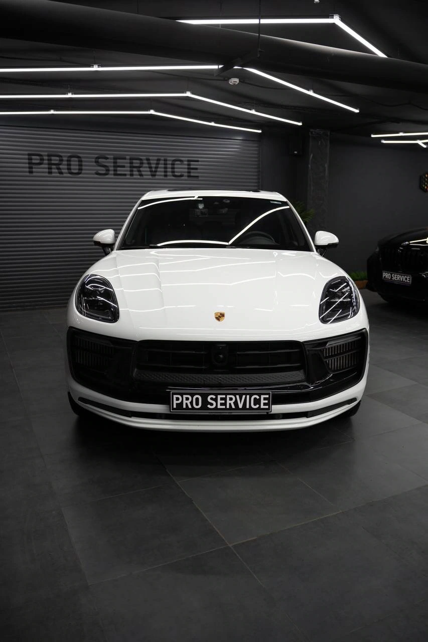 Белый Porsche Macan, прямой вид спереди: капот, фары и чёрные элементы переднего бампера.