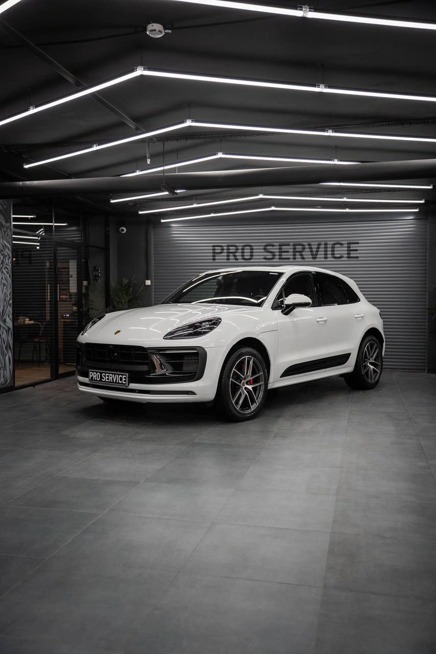 Белый Porsche Macan, вид спереди под углом в освещённом боксе студии.