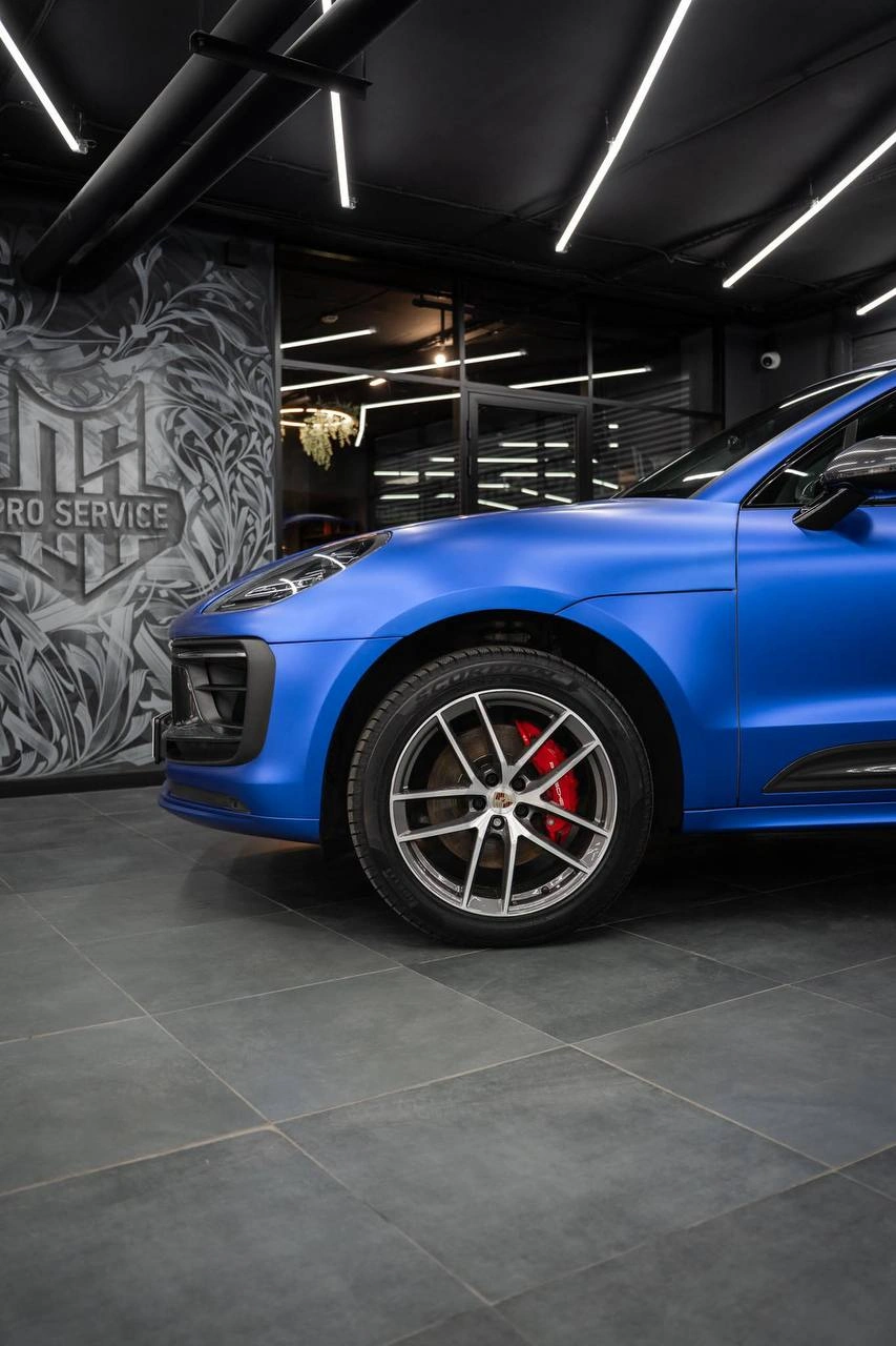 Передняя боковая часть синего Porsche Macan: колесо, красный суппорт и синяя кузовная панель.