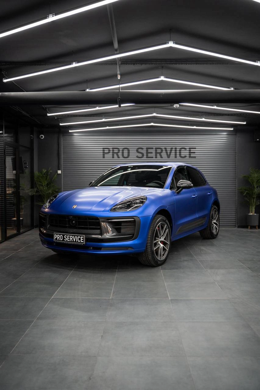 Синий Porsche Macan, общий вид спереди под углом на фоне ворот студии.