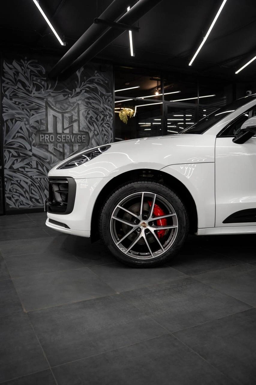 Передняя боковая часть белого Porsche Macan: колесо, красный суппорт и край переднего бампера.