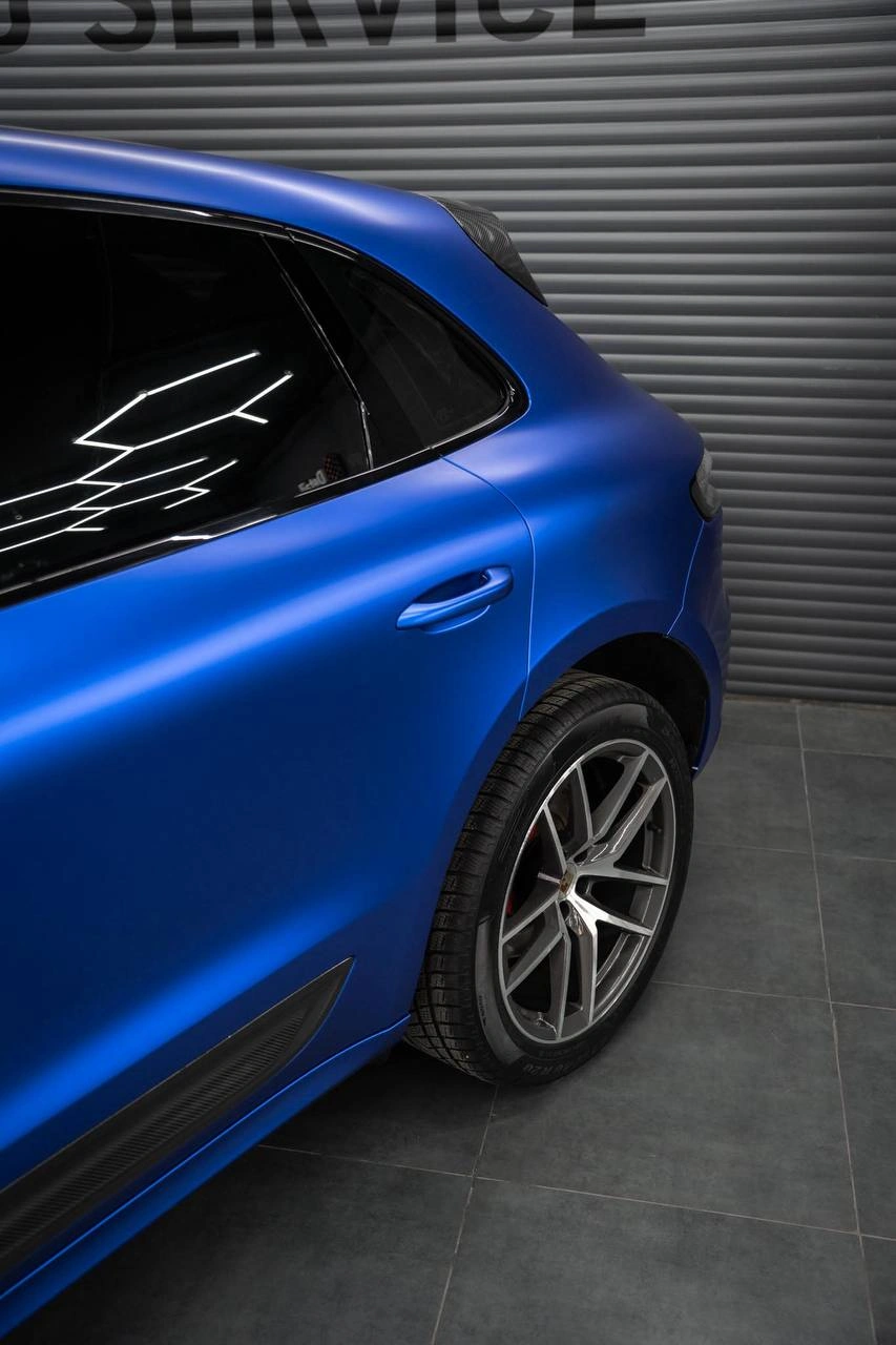 Боковая часть синего Porsche Macan: двери, заднее окно и заднее колесо крупным планом.