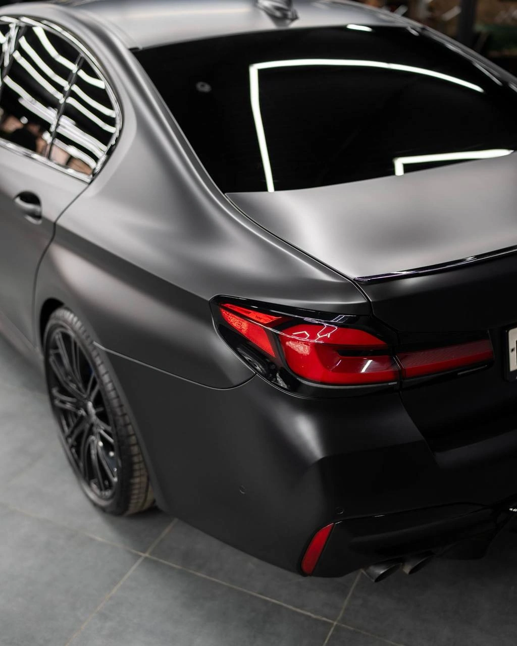 Задний фонарь и крышка багажника BMW 5 G30 крупным планом, на тёмном кузове отражаются световые линии.