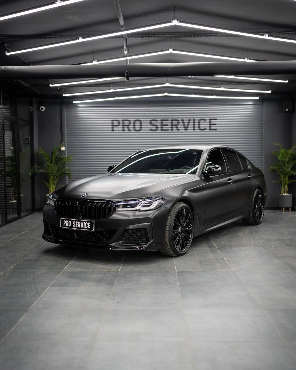 Тёмный BMW 5 G30 в боксе PRO Service: кузов и передняя часть под ровными линиями потолочного света.