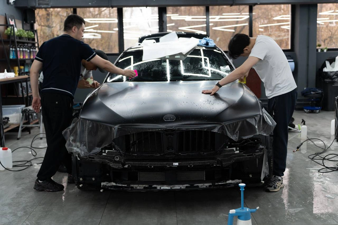Мастера натягивают матовую защитную плёнку на капот BMW 5.