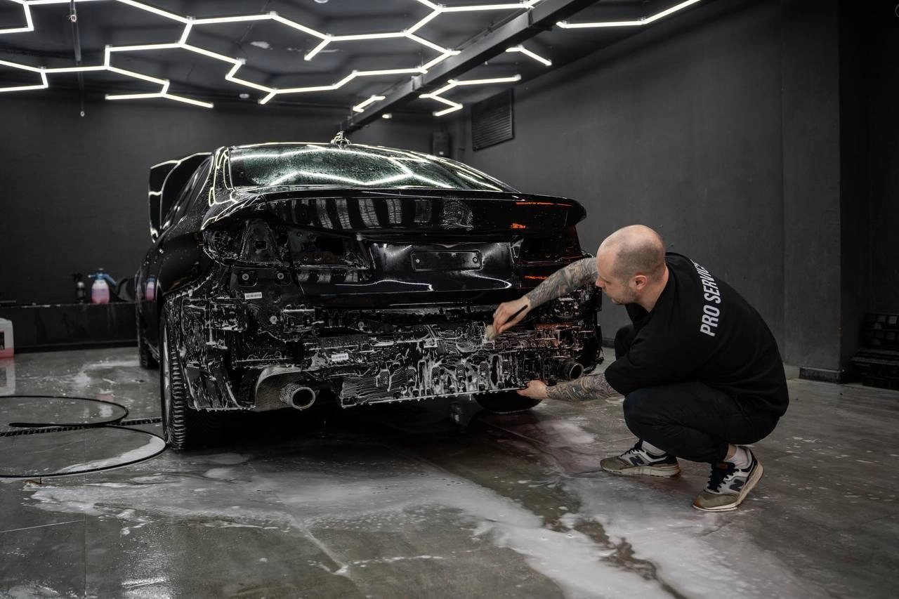 Мастер очищает заднюю часть BMW 5 со снятым бампером перед дальнейшими работами.