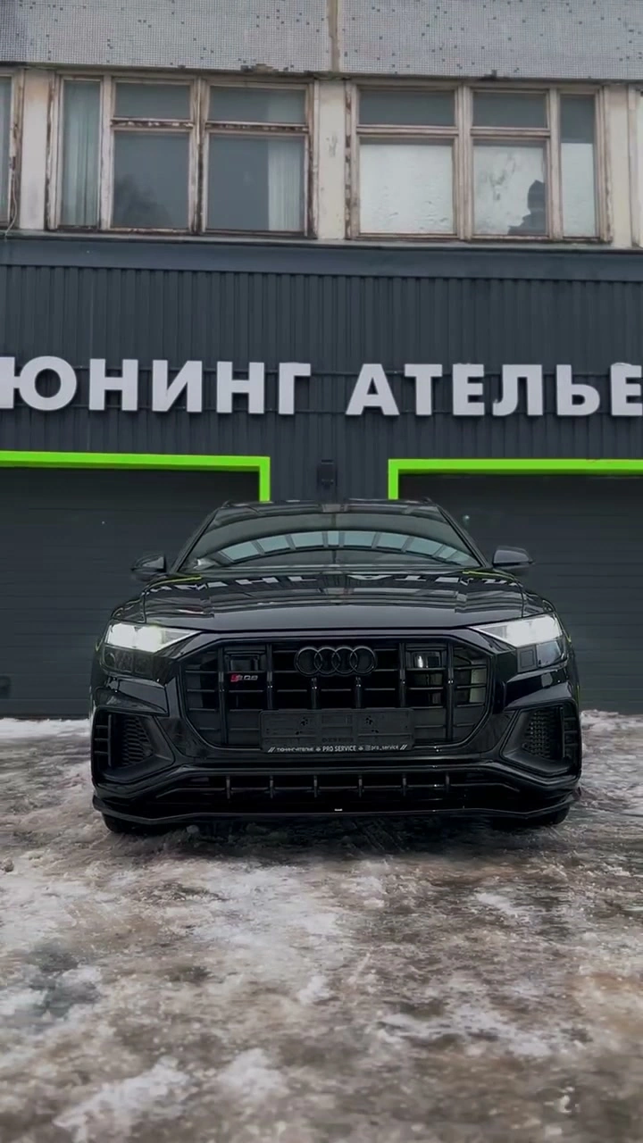 Кадр из видео: Audi SQ8 перед зданием ателье — вид спереди на тёмную решётку радиатора и фары.
