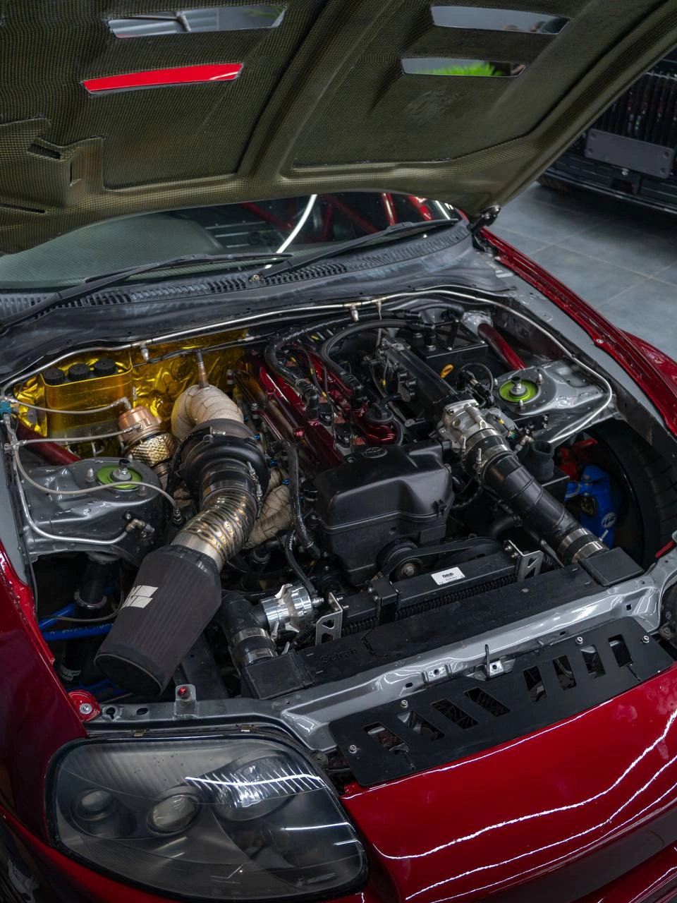 Открытый моторный отсек Toyota Supra: двигатель и патрубки под поднятым капотом.