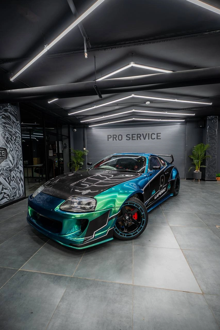 Toyota Supra с бирюзовой гоночной графикой, вид спереди под углом в освещённом боксе студии.
