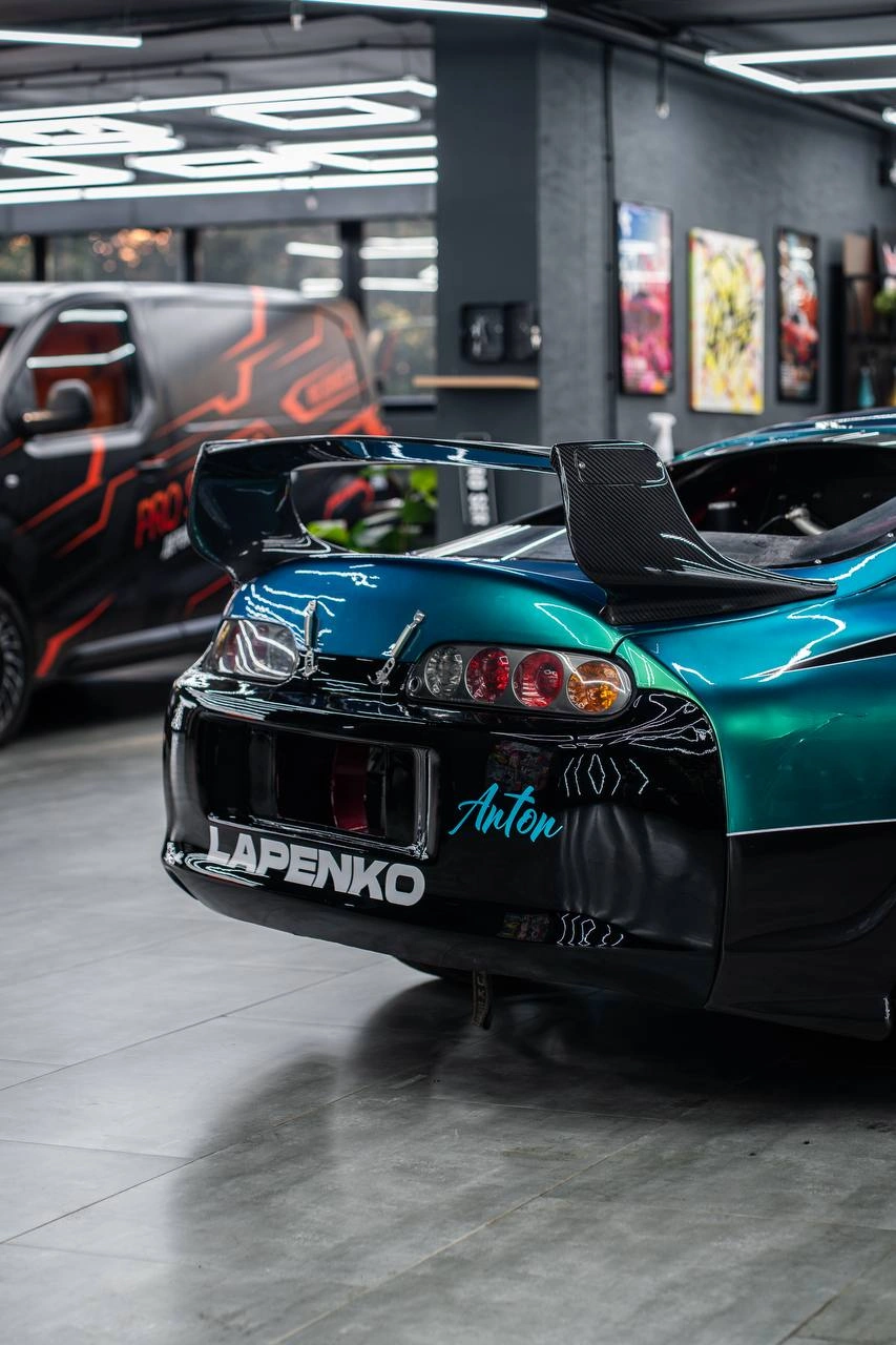 Задняя часть Toyota Supra: круглая оптика, высокий чёрный спойлер и бирюзово-чёрная графика.