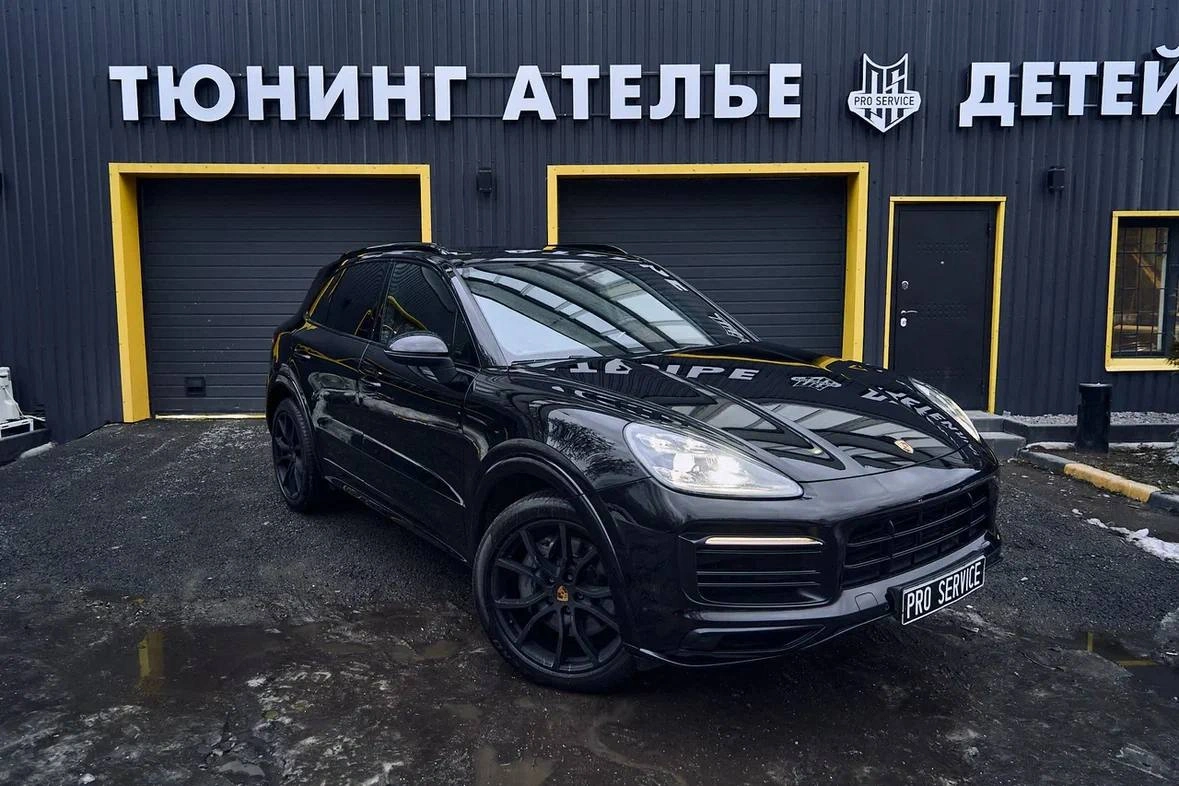 Porsche Cayenne — чёрный кроссовер спереди под углом на площадке перед тюнинг-ателье